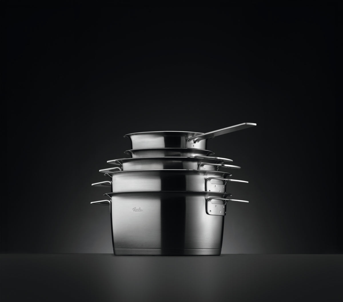Fissler Phi Collection® Stielkasserolle und Kochgeschirr, Edelstahl, präzise gefertigt in Deutschland. Dramatische Beleuchtung unterstreicht die Qualität.