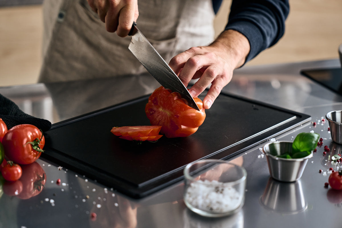 Eine Person schneidet eine Tomate mit dem präzisionsgefertigten Fissler ProCut Kochmesser 20cm auf einer schlichten, modernen Küchenzeile.