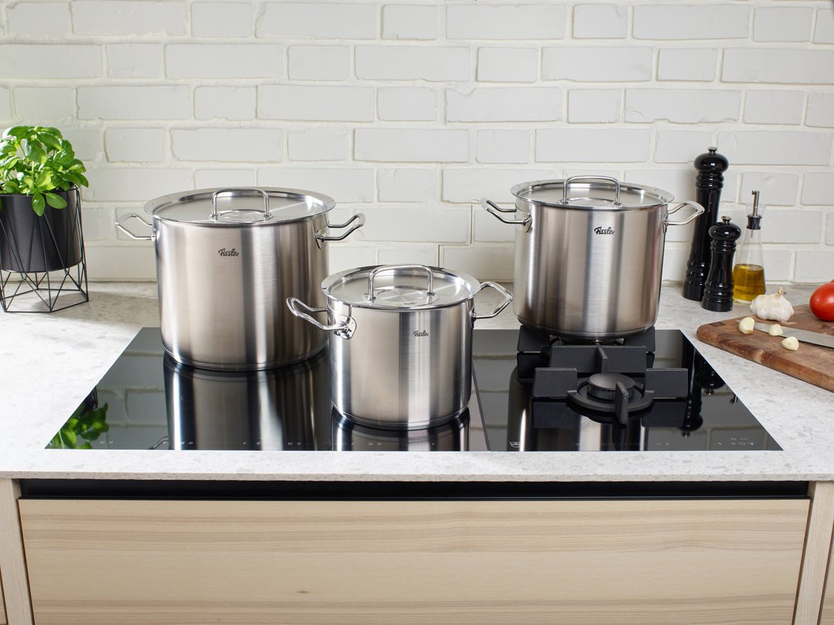 Drei Fissler Original-Profi Collection® Edelstahl-Kochtöpfe mit Deckel auf Herd; modern, langlebig, präzise gefertigt.