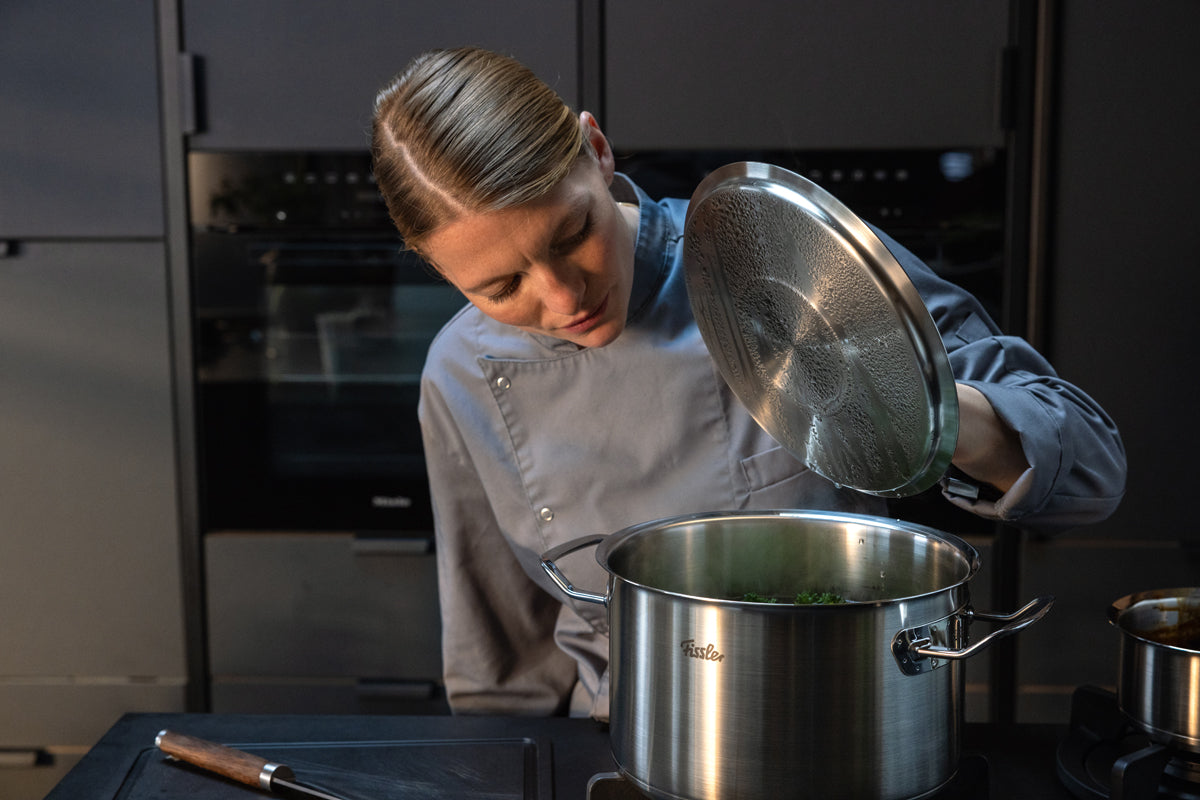 A chef checks vegetables in a pot from the Fissler Original-Profi Collection® - a modern kitchen setting made of German stainless steel.