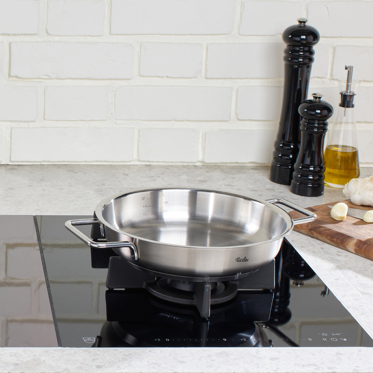 A Fissler Pure serving pan made in Germany sits on a gas stove in a modern kitchen with high-quality cookware nearby.