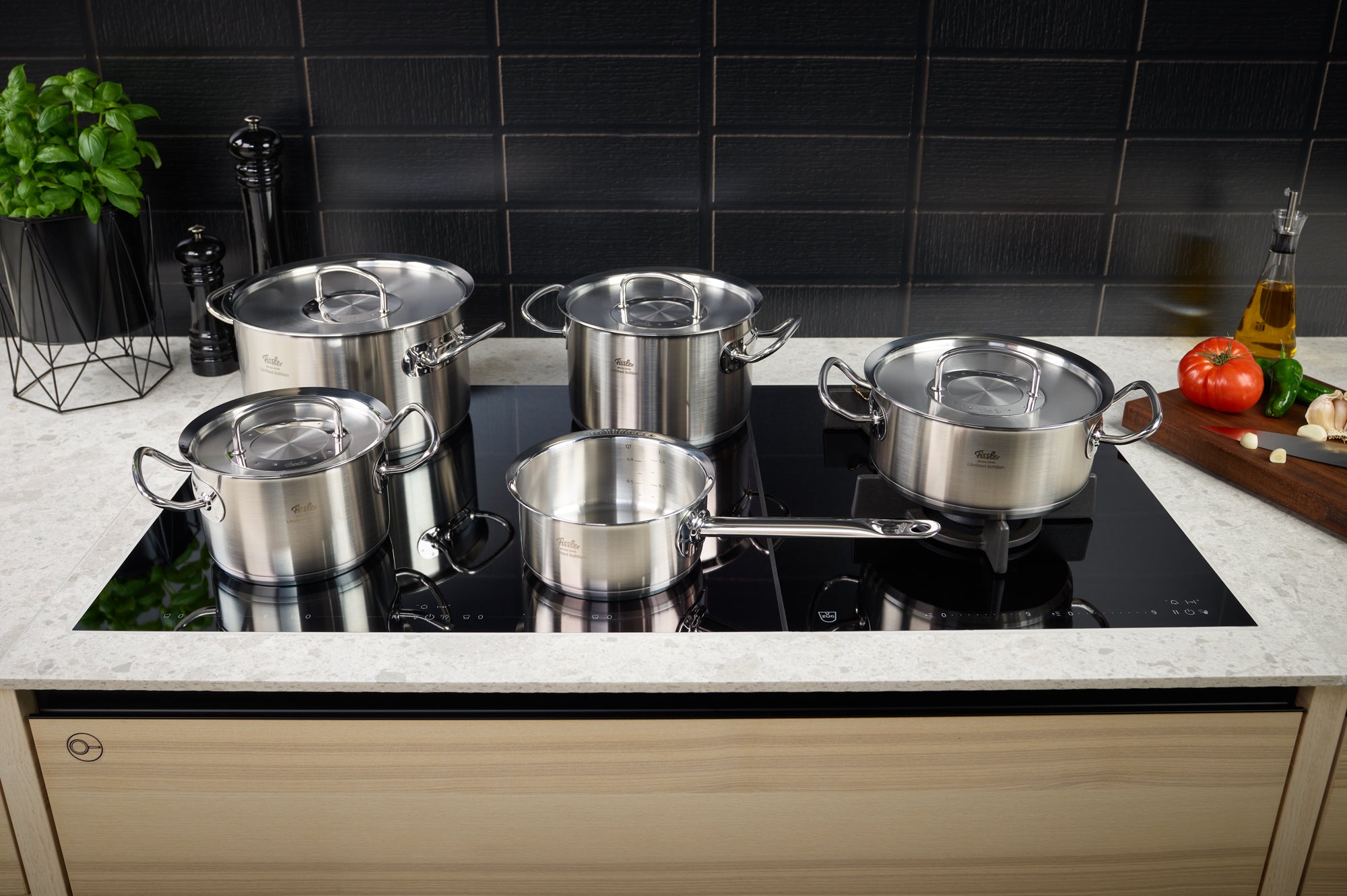 Fissler Original-Profi Collection® Retro 5-piece stainless steel set on an induction hob, with fresh ingredients and utensils nearby.