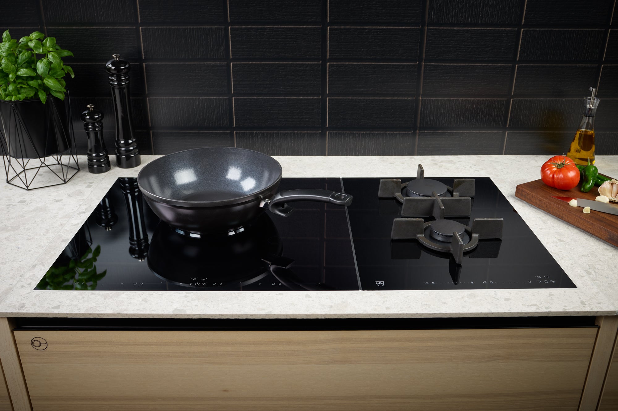 Eine moderne Küche mit dem Fissler Ceratal® Wok Orbitschwarz auf einem Glaskochfeld, frischen Kräutern und küchenfertigem Gemüse.