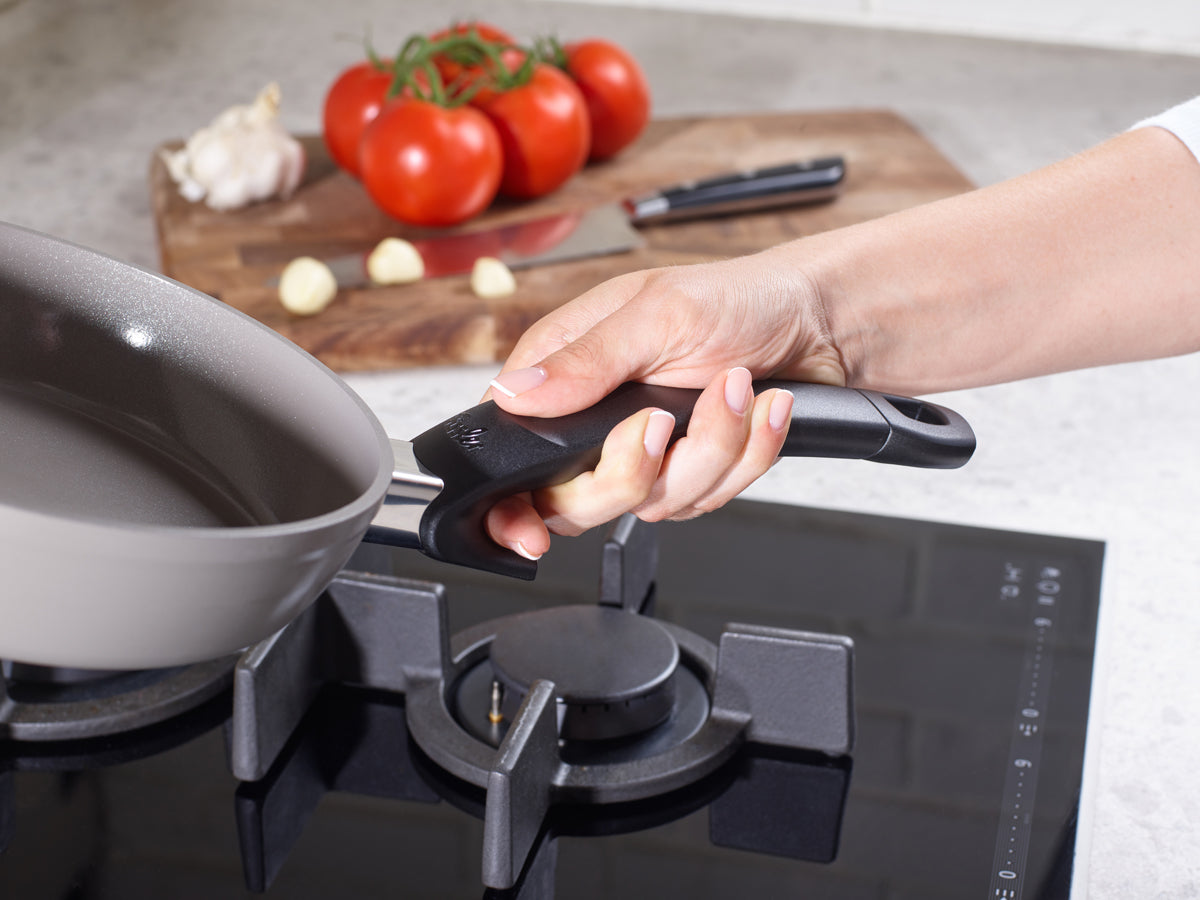 Ein schwarzer Griff ist an einer Fissler Ceratal®-Pfanne befestigt, die auf einem Gasherd steht, mit frischen Zutaten und Qualität aus deutscher Produktion.