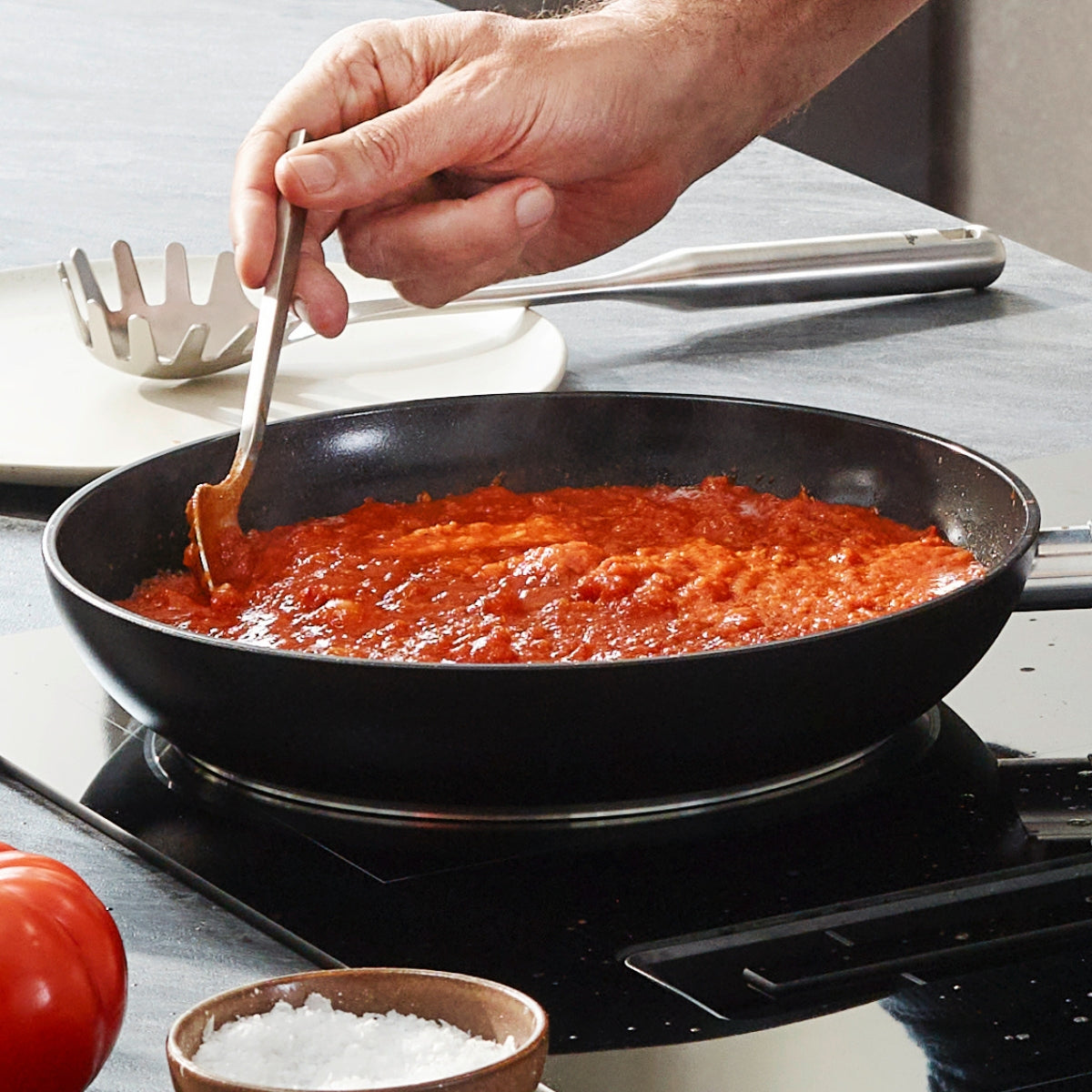 A hand stirs tomato sauce in a Fissler Essential® Frying Pan on the stove - modern, PFAS/PTFE-free, quality "Made in Germany".