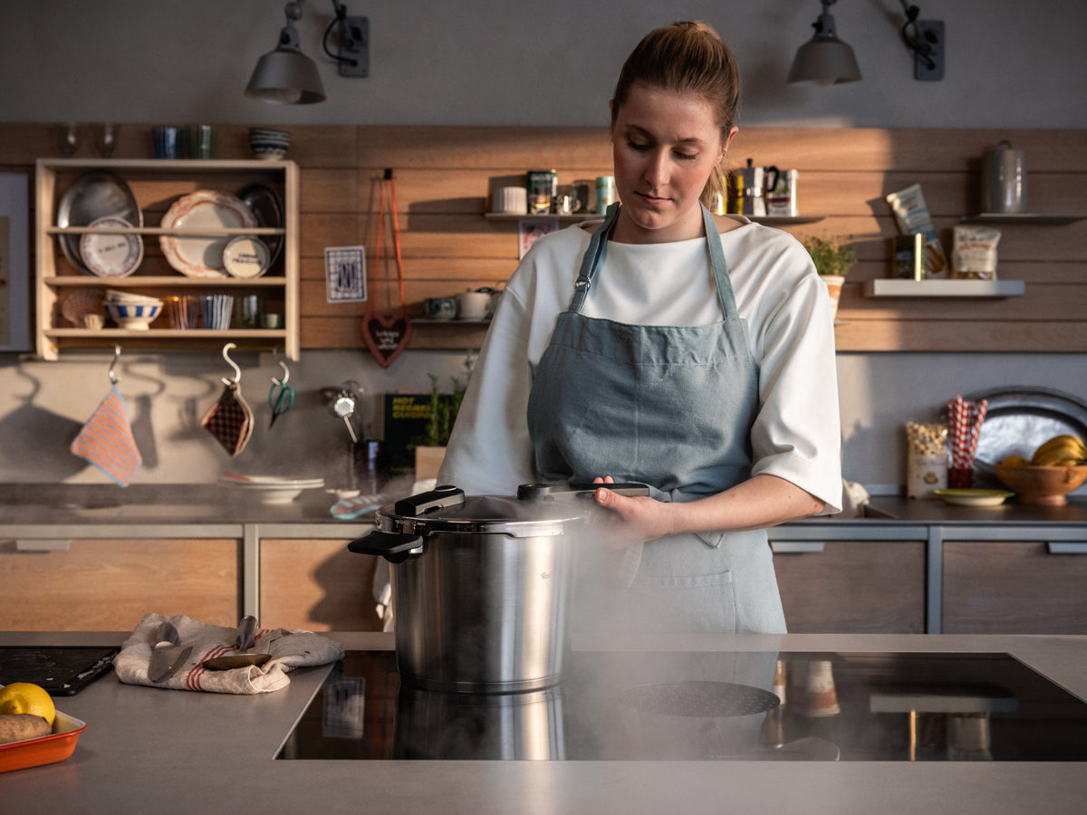 In einer hellen Küche benutzt eine Frau das Fissler Vitaquick® Premium Schnellkochtopf-Set - präzises Kochgeschirr "Made in Germany" in Aktion.