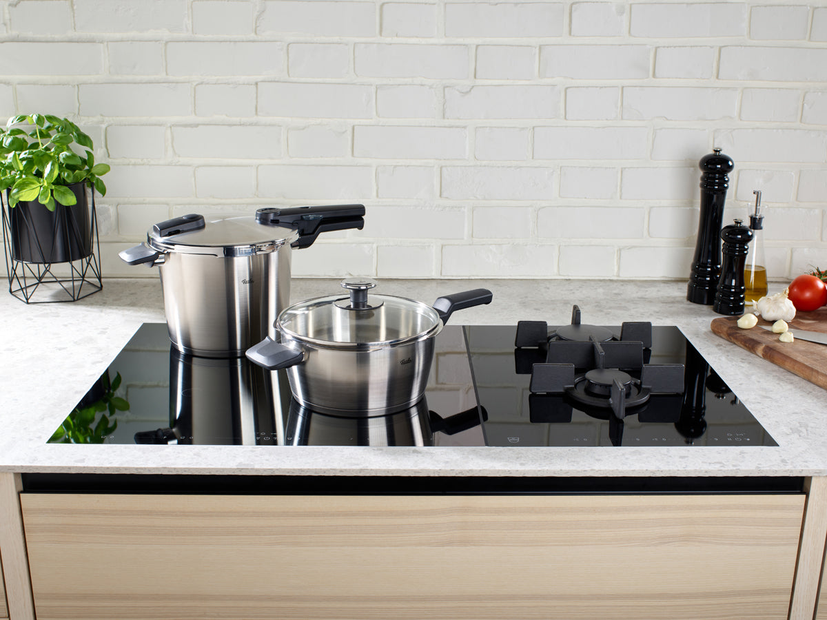 Fissler Vitaquick® Premium 2-piece Pressure Cooker Set on black glass hob; high-quality German cookware in a stylish kitchen setting.