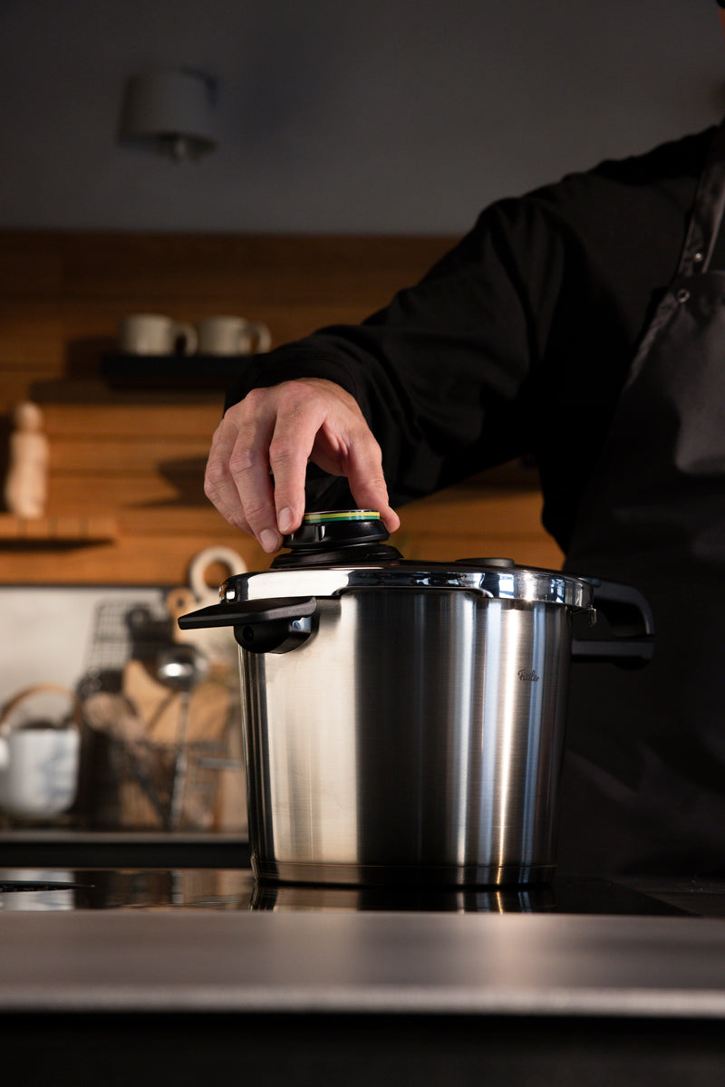 Ein Koch befestigt den Deckel eines Fissler Vitavit® Premium-Sets - eines in Deutschland hergestellten Schnellkochtopfs aus Edelstahl - auf einer modernen Küchenzeile.