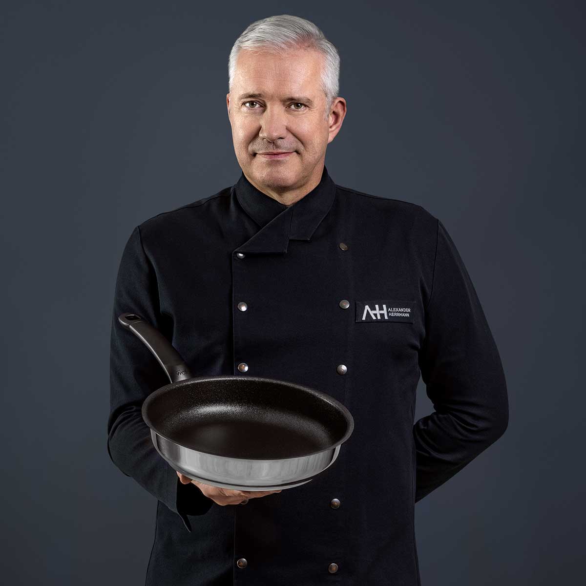 A chef in black presents the Fissler Adamant® Premium Frying Pan - Made in Germany, scratch-resistant and built to last.