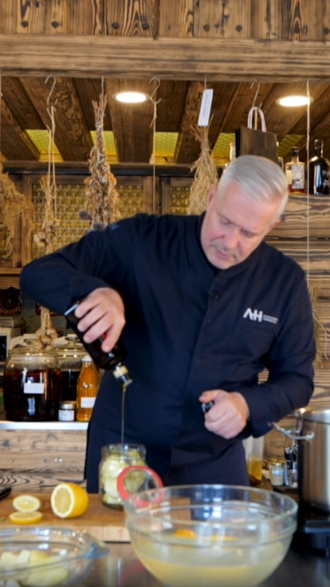 A chef uses Fissler cookware in a rustic kitchen, pouring oil over lemons, surrounded by high-quality stainless steel pots and tools.