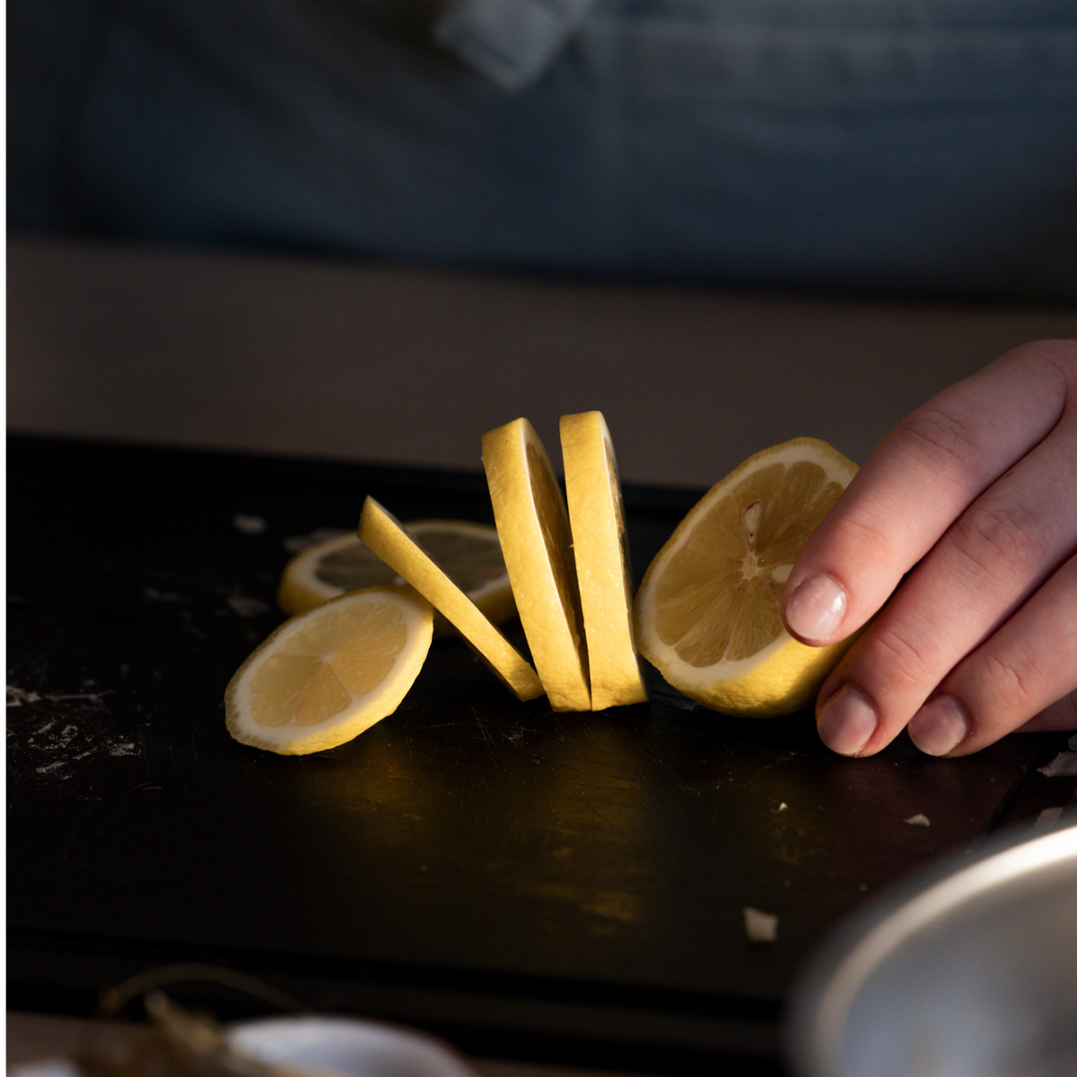 A hand expertly slices a lemon on a sleek black Fissler cutting board, showcasing precision and control. Several fresh lemon slices rest on the board, reflecting the brand’s commitment to quality kitchen accessories designed for durability and timeless elegance.