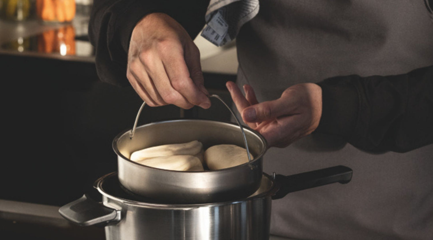 Eine Person dünstet Teig in einem Fissler-Edelstahleinsatz über einem Kochtopf und präsentiert damit deutsches Präzisionskochgeschirr in einer modernen Küche.