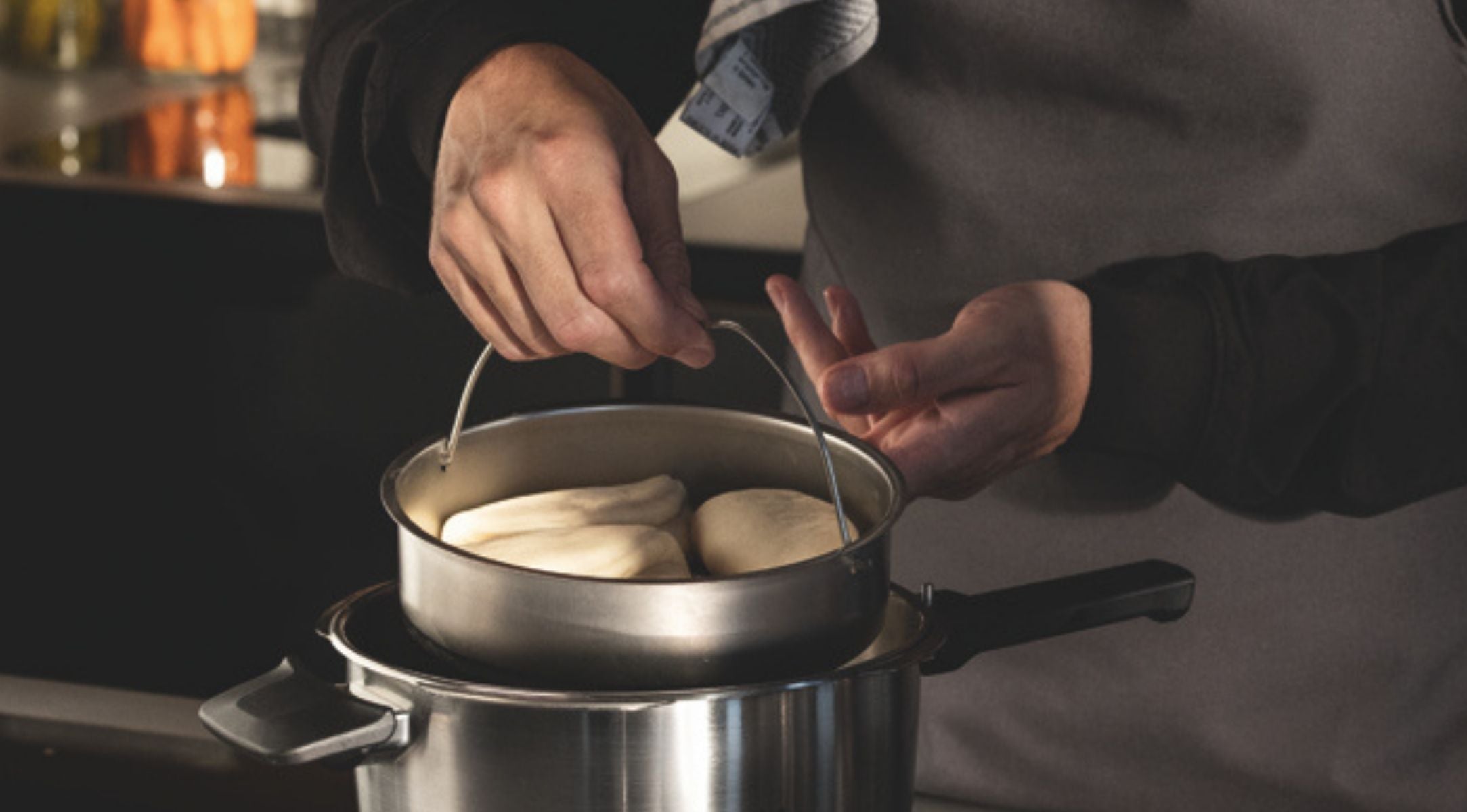 Eine Person dünstet Teig in einem Fissler-Edelstahleinsatz über einem Kochtopf und präsentiert damit deutsches Präzisionskochgeschirr in einer modernen Küche.