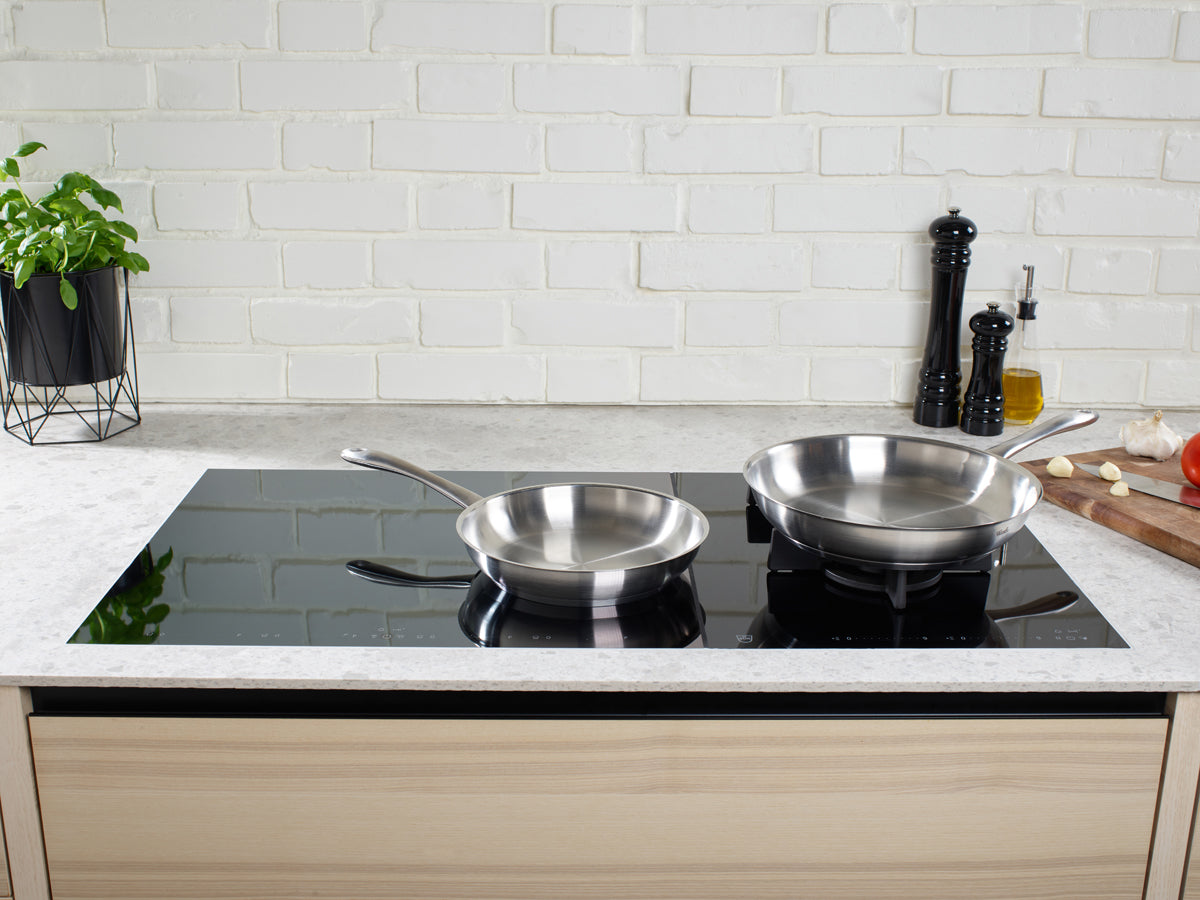 Zwei Fissler Catania Pfannen auf einem eleganten Induktionskochfeld in einer modernen Küche - zeitloses deutsches Design, gemacht für den Alltag.