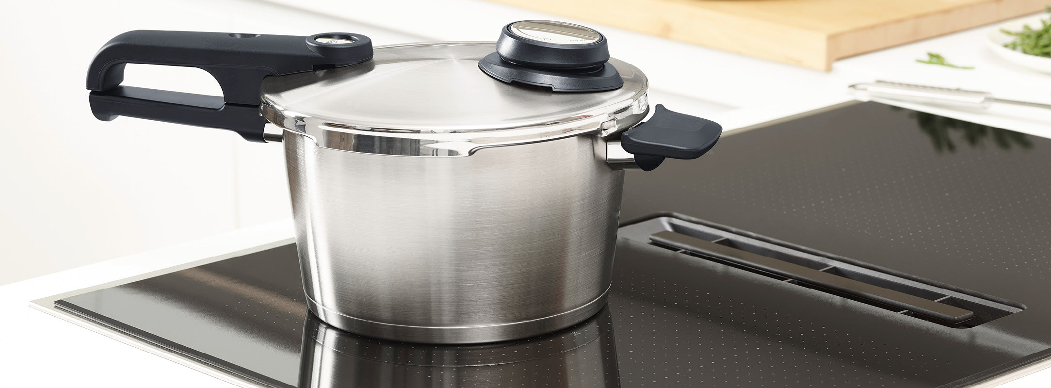 Ein Fissler-Schnellkochtopf aus Edelstahl mit schwarzen Griffen und Manometer auf einer eleganten elektrischen Herdplatte in einer hellen Küche.