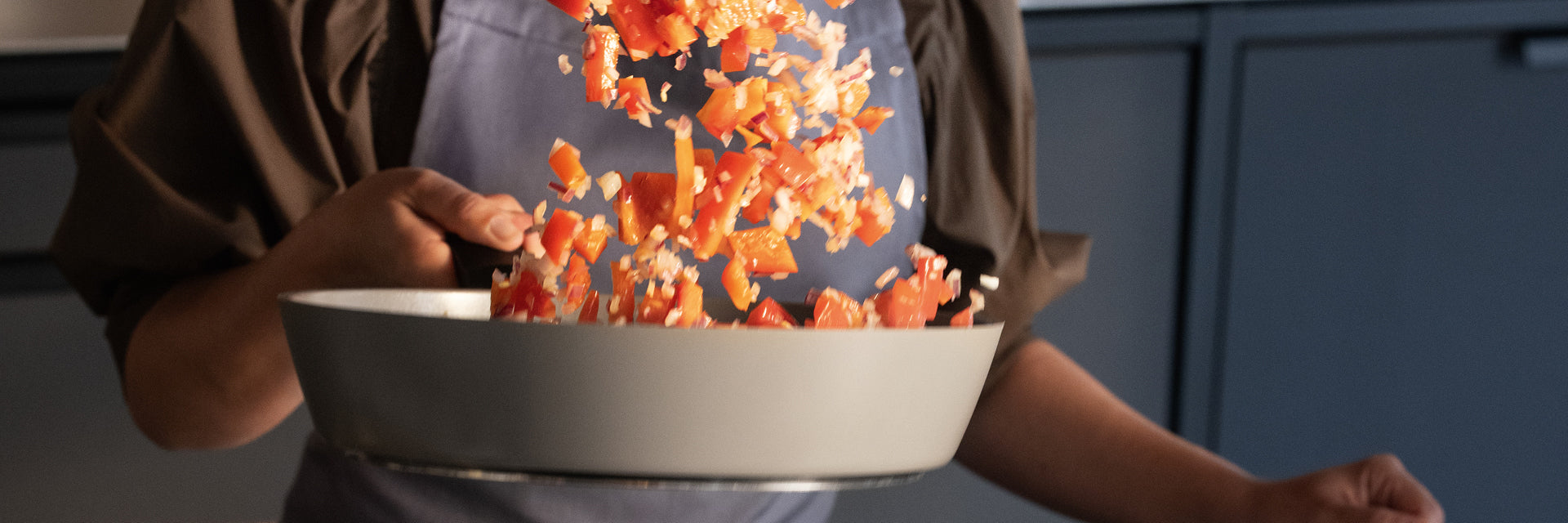 Eine Person brät rote Paprika und Zwiebeln in einer hochwertigen Fissler-Edelstahlpfanne, die deutsche Qualität und zeitloses Design verkörpert.