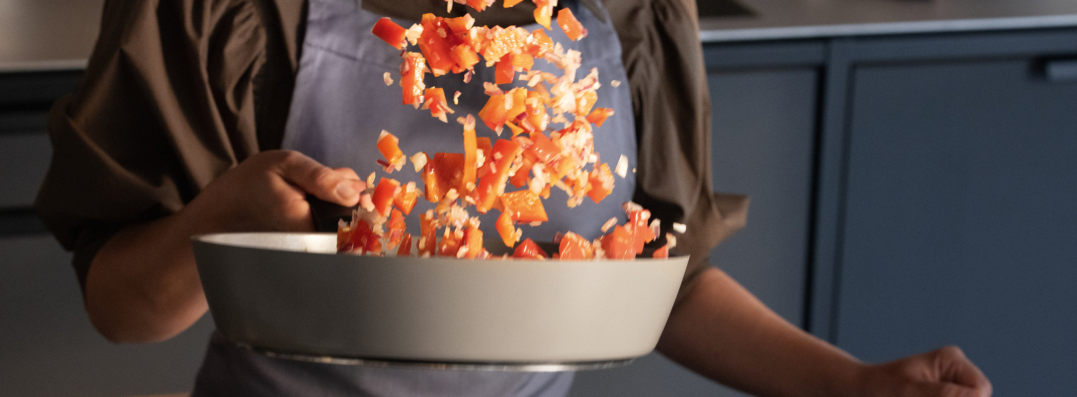 Eine Person in einer Schürze brät rote Paprika und Zwiebeln in einer hochwertigen Fissler-Pfanne an und zeigt damit deutsche Qualität in der Küche.