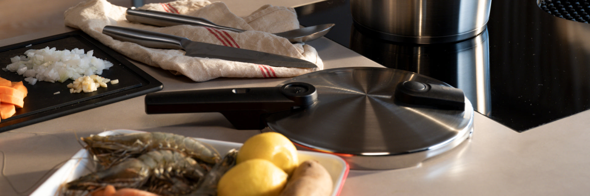 Eine Küchentheke mit einem Fissler-Schnellkochtopfdeckel, einem rostfreien Topf, Messern und frischen Zutaten, die zum präzisen Kochen vorbereitet sind.