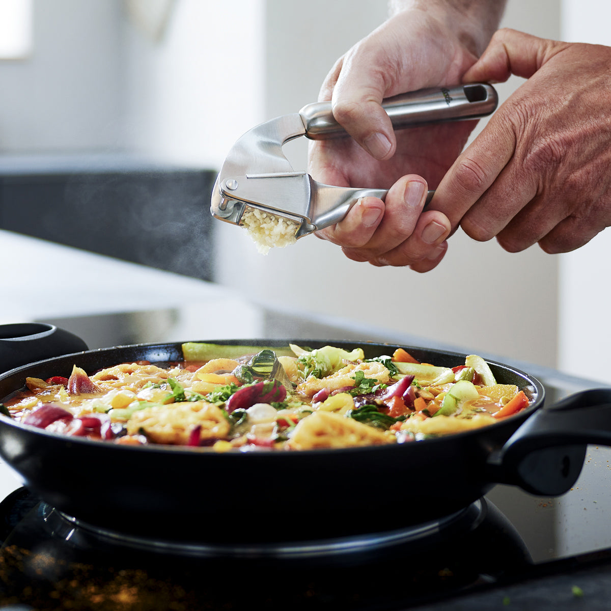 Frischer Knoblauch wird in einer Fissler-Pfanne mit lebhaftem Gemüse und Soße gepresst und auf dem Herd gedünstet, um eine präzise und hochwertige Zubereitung zu gewährleisten.