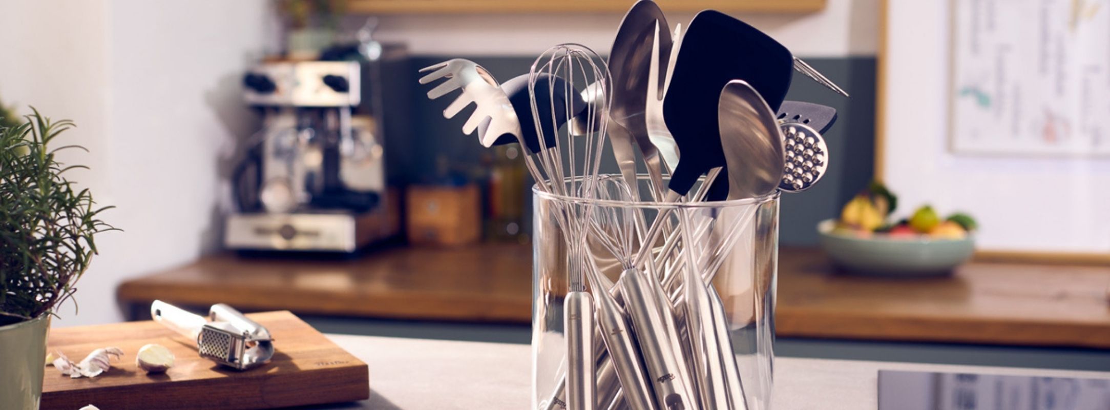 Utensilien aus rostfreiem Stahl von Fissler - Schneebesen, Pfannenwender, Schöpflöffel und Nudelservierer - stehen elegant auf einer Küchenzeile.