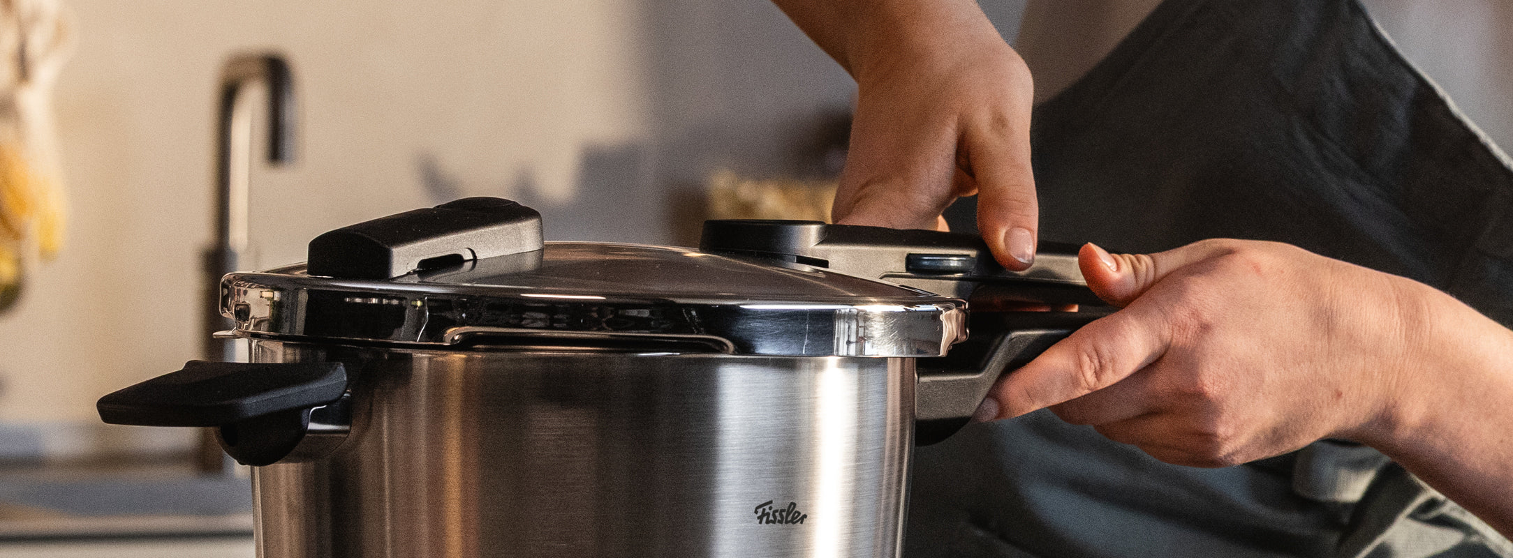 Eine Person befestigt den Deckel eines Fissler Edelstahl-Schnellkochtopfs in einer modernen Küche und ist bereit, deutsche Präzisionsküche zu genießen.