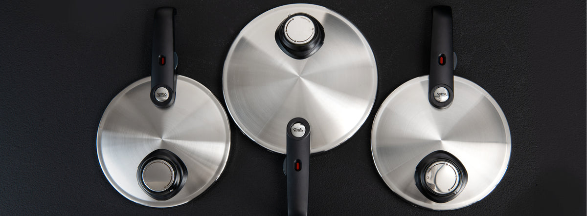 Three Fissler stainless steel pot lids with characteristic black knobs, arranged on a dark surface - precision meets timeless design.