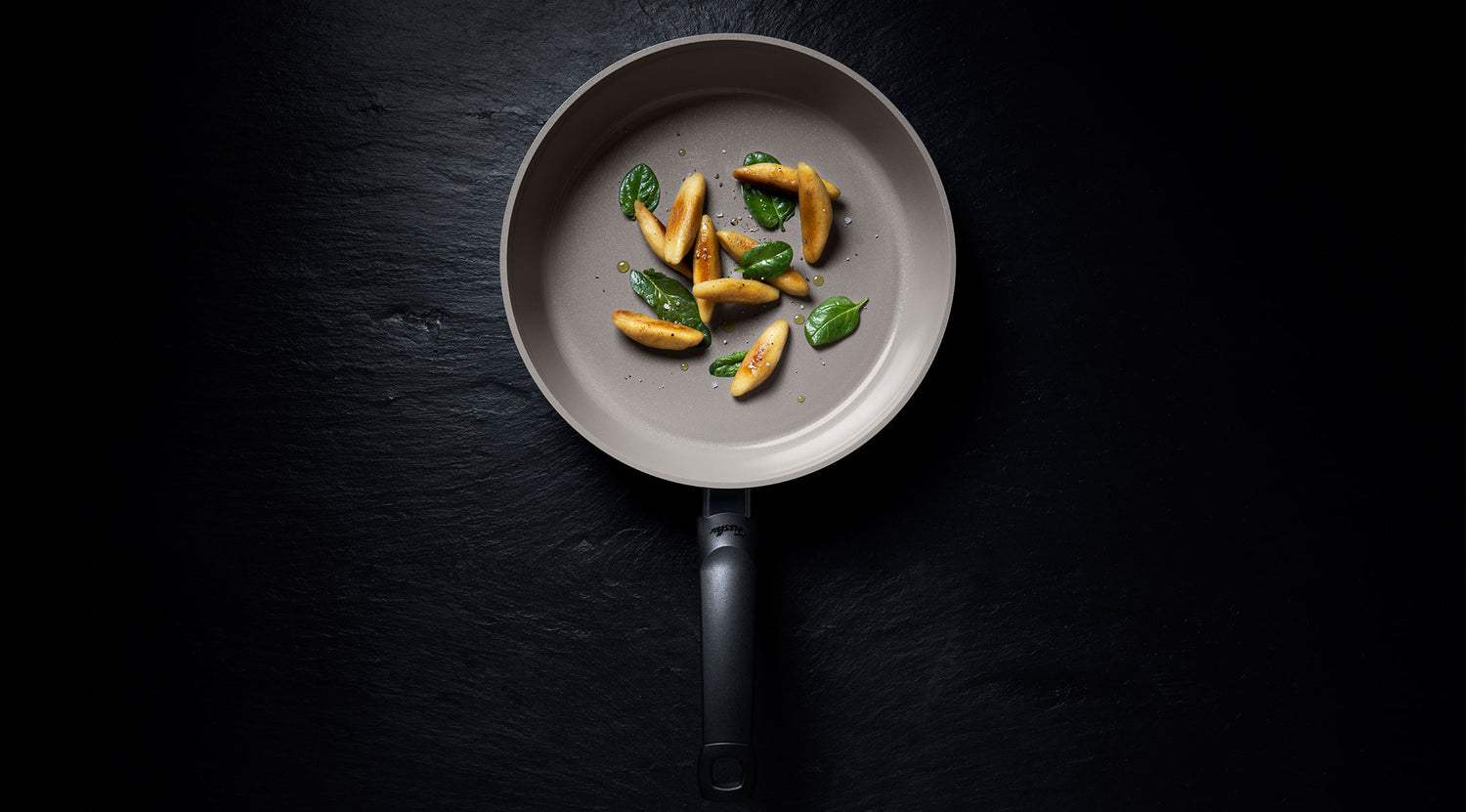 Fissler Antihaft-Pfanne auf dunkler Oberfläche mit goldbraunen Gnocchi und Basilikum, die von deutscher Präzision und zeitlosem Design zeugt.
