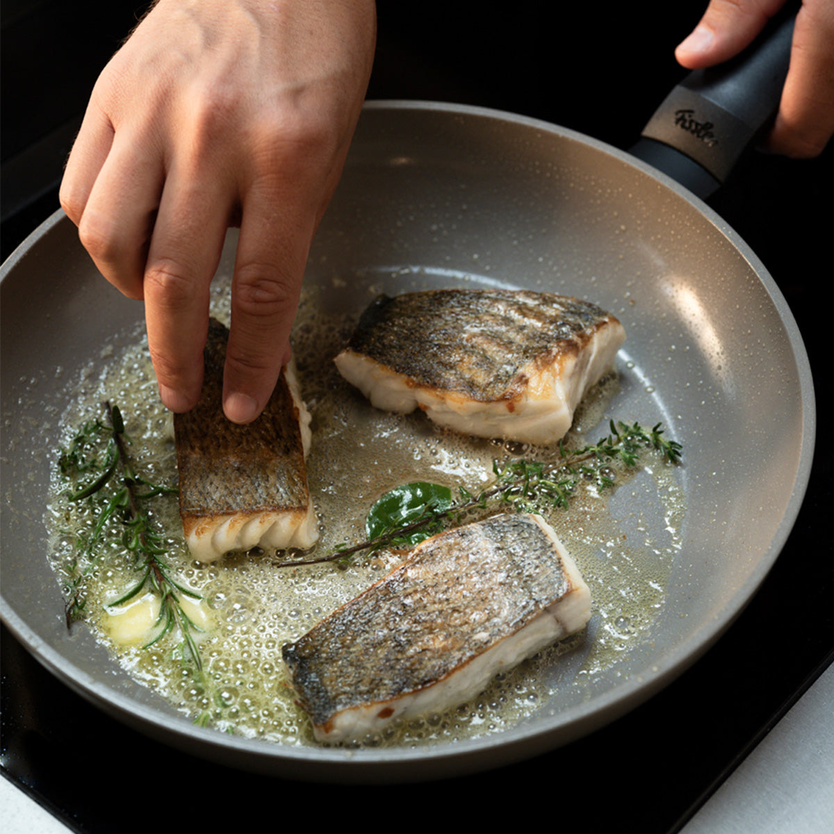Experience precision cooking with the Fissler Ceratal® Evo Classic Pfanne: three pieces of skin-on fish are expertly prepared with herbs and butter, while a hand carefully adjusts one fillet. Superior German engineering and innovation ensure even heat distribution for perfect results—hallmarks of Fissler’s heritage in premium cookware since 1845.