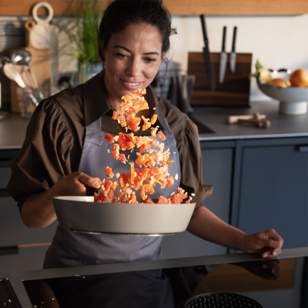 Eine Frau verwendet ein Fissler Ceratal® Evo Comfort-Pfannenset und schwenkt voller Freude Gemüse in einer modernen Küche – Präzision „Made in Germany“.