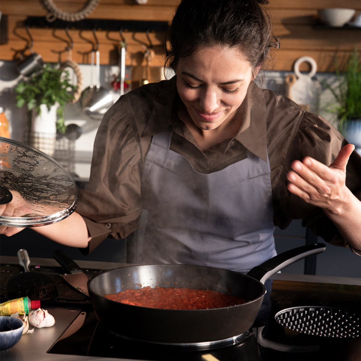 Eine Frau lächelt, hebt den Deckel der Fissler Ceratal® Evo Comfort-Pfannen an und genießt die Qualität „Made in Germany“ sowie das zeitlose Design.