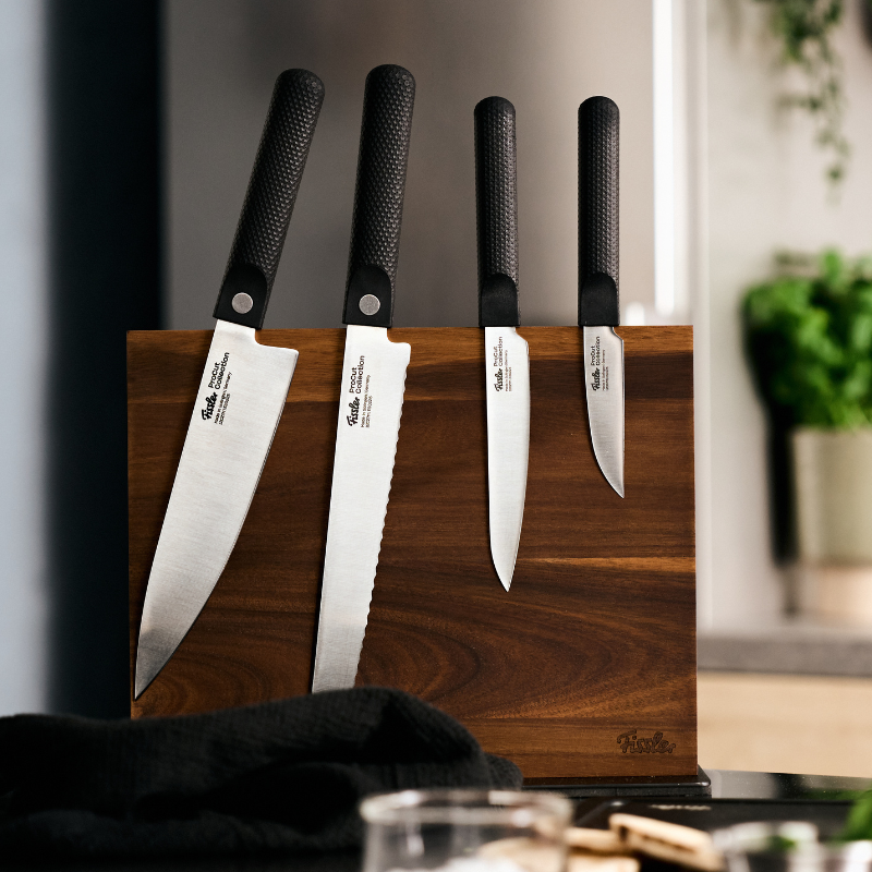Vier hochwertige Fissler-Messer mit schwarzen Griffen in einem Holzblock auf einer Küchenarbeitsplatte, die an deutsche Präzision und zeitloses Design erinnern.