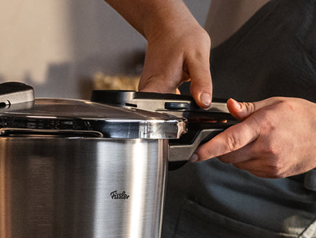 Die Hände sichern den Deckel des Fissler Vitaquick® Premium Schnellkochtopf-Sets, das in Deutschland für sicheres und schnelles Kochen hergestellt wird.