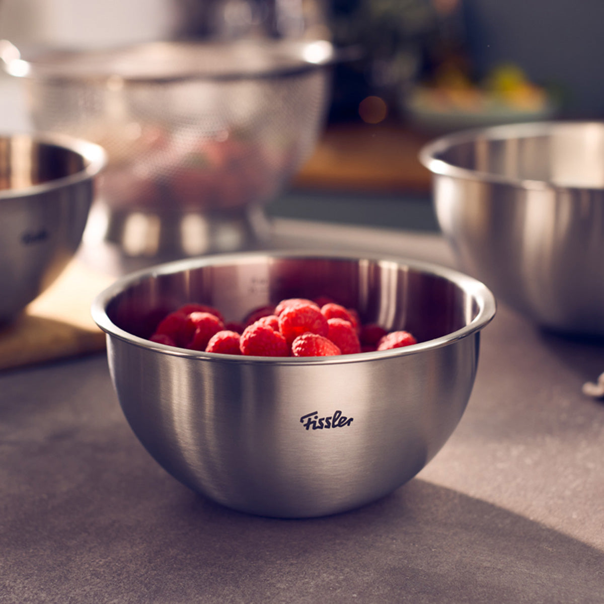 Die Fissler Essential® 16cm Edelstahlschüssel, gefüllt mit Himbeeren, auf der Arbeitsplatte neben weiteren Schüsseln.