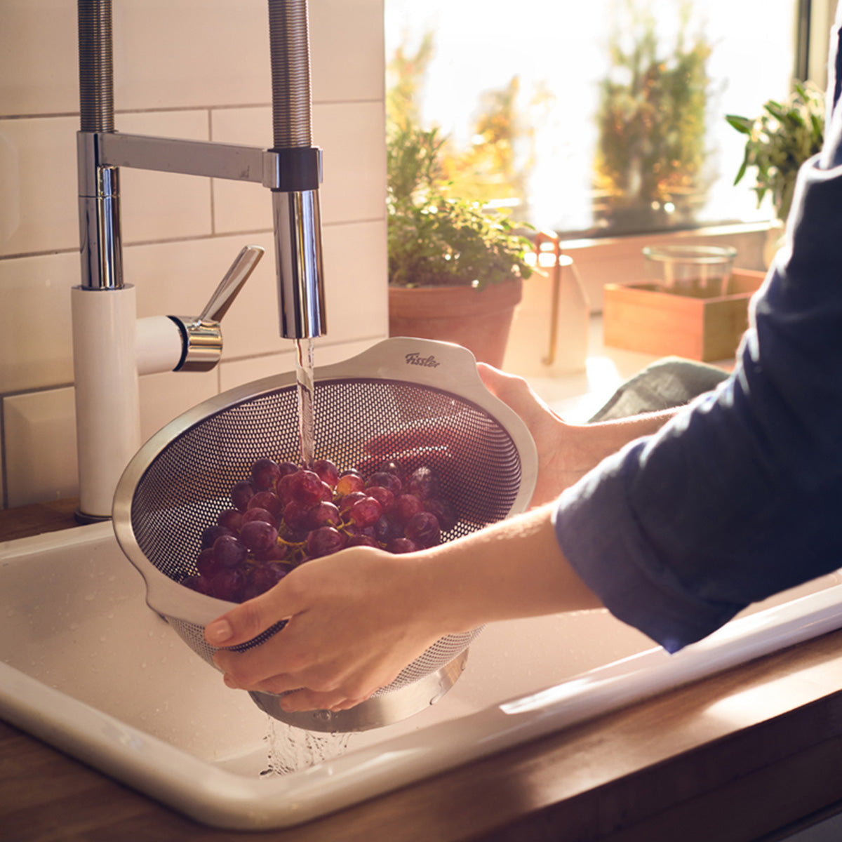 Rote Trauben, gewaschen in einem Fissler Essential® Sieb 24cm, Sonnenlicht durch das Fenster - deutsches Präzisionsdesign für frische, saubere Früchte.