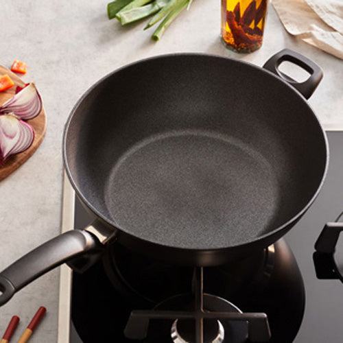 Fissler Adamant® Wok mit langlebiger Antihaftbeschichtung auf der Herdplatte, Gemüse und Öl in der Nähe - deutsches Präzisionskochgeschirr seit 1845.