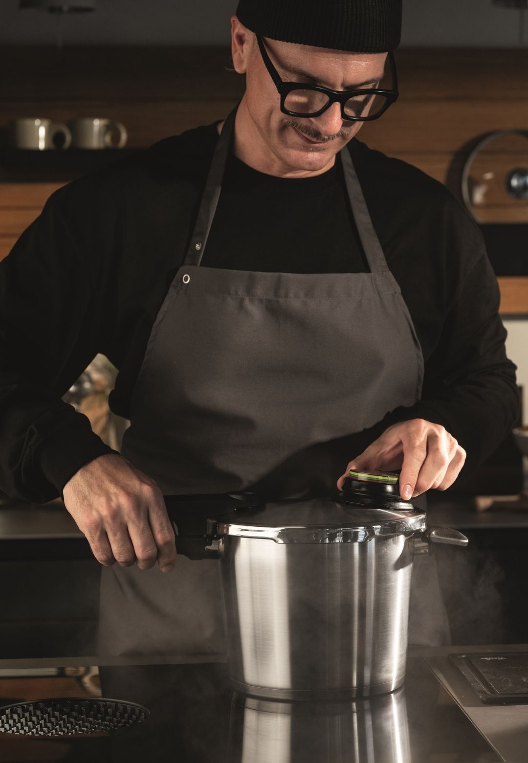 Eine Person in einer modernen Küche öffnet einen dampfenden Fissler-Schnellkochtopf auf der Herdplatte, der zeitloses deutsches Design präsentiert.