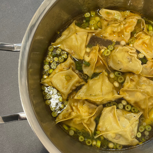 In einem Fissler-Edelstahltopf köcheln Wontons in Brühe, garniert mit grünen Zwiebeln - Präzision, Haltbarkeit und Innovation.