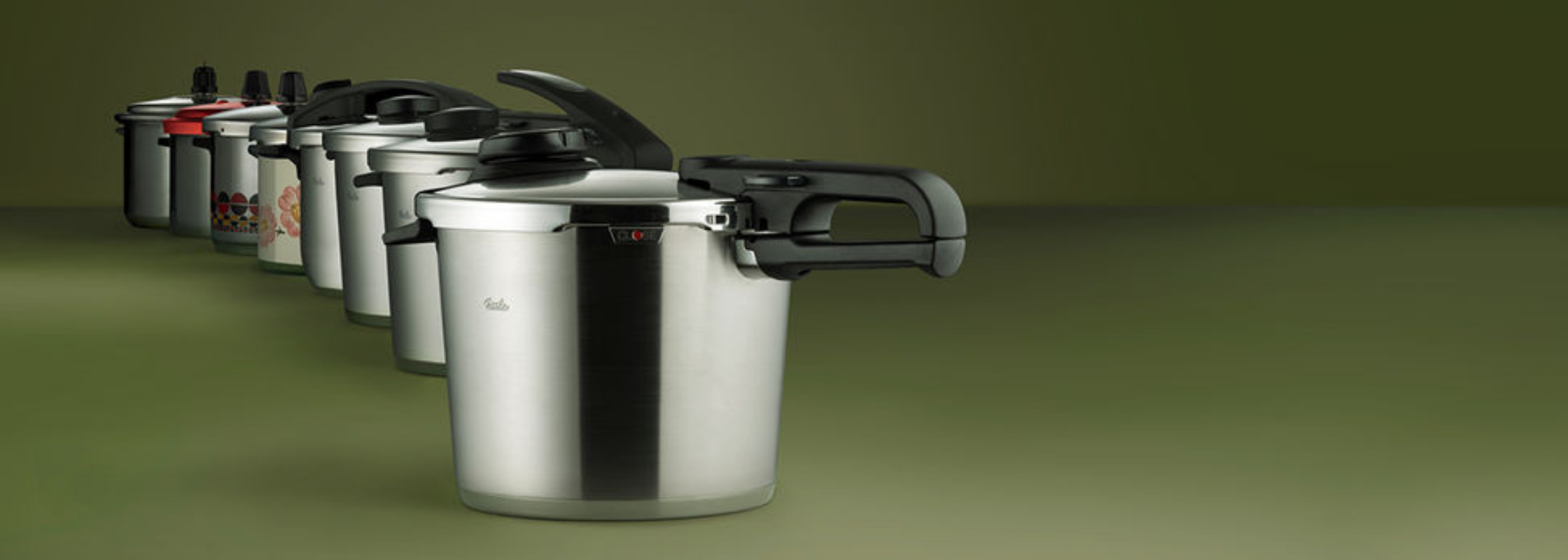 Sechs Fissler Schnellkochtöpfe aus rostfreiem Stahl in einer diagonalen Reihe, jeder mit einzigartigem, in Deutschland entwickeltem Deckel- und Griffdesign.