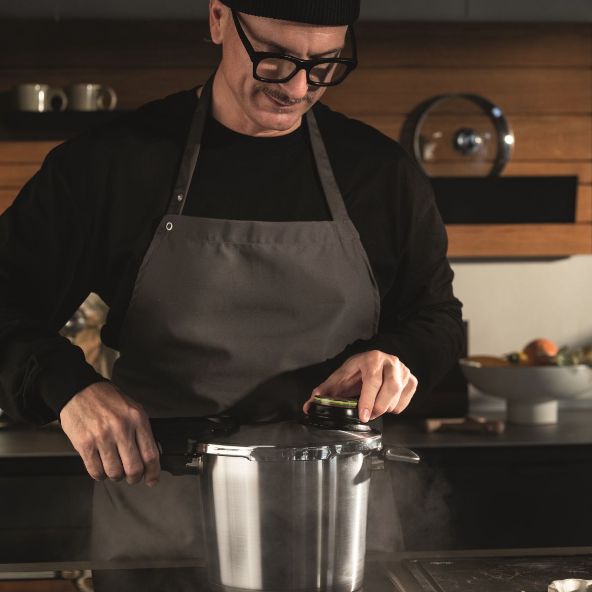 Eine Person in einer modernen Küche öffnet vorsichtig einen Fissler Schnellkochtopf aus rostfreiem Stahl und lässt Dampf entweichen - Präzision und Qualität in Aktion.