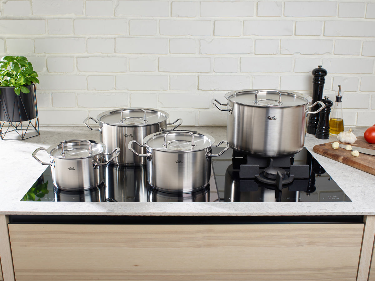 Fissler Original-Profi Collection® 5-piece set on a modern stove, surrounded by vegetables. Stainless steel, "Made in Germany", dishwasher safe.