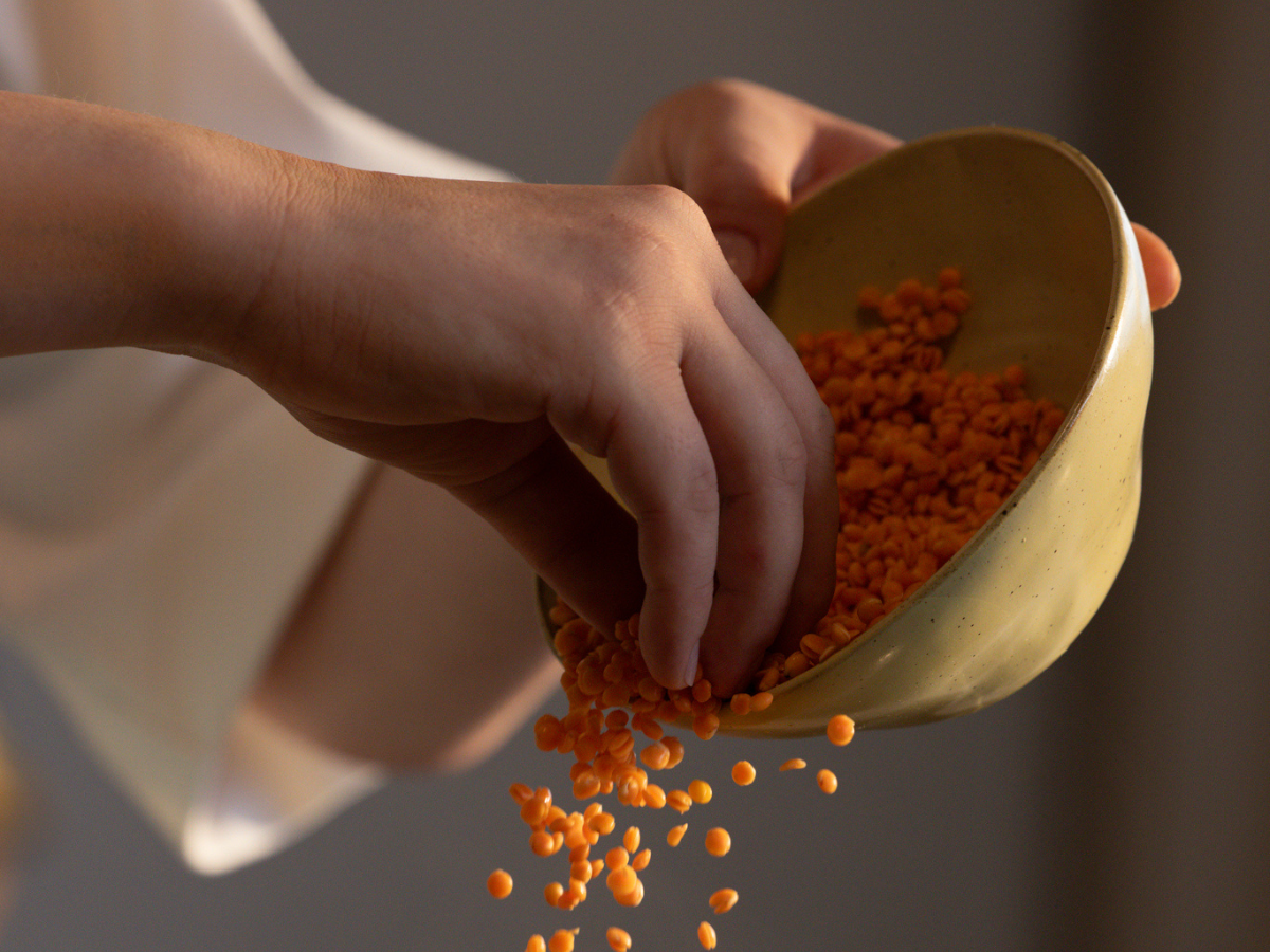 A hand pours vibrant orange lentils from a softly curved light brown bowl, the grains cascading gracefully in midair. The scene reflects Fissler’s commitment to premium quality kitchenware—timeless design and precision for effortless cooking.