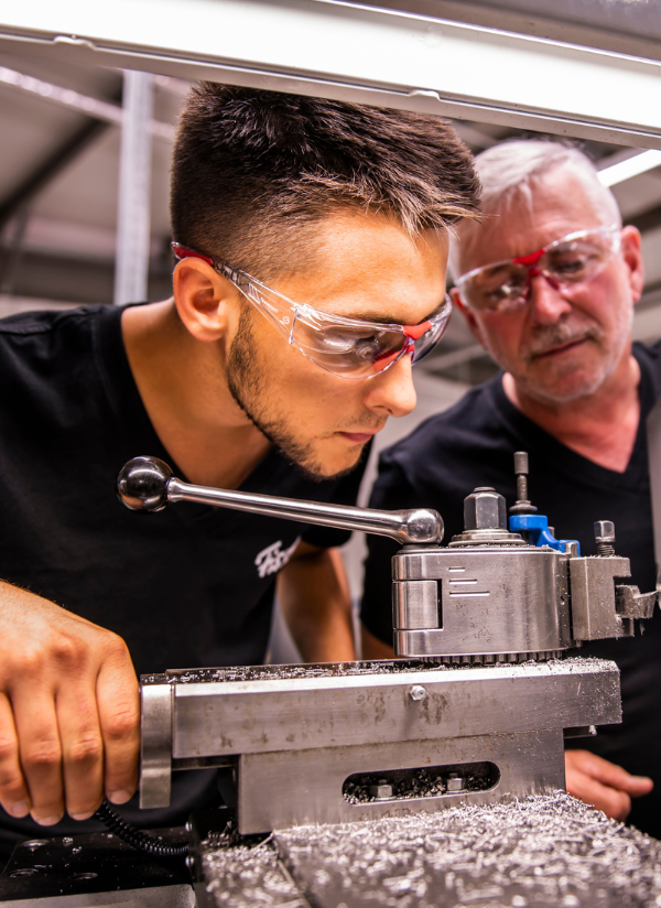 In einer deutschen Werkstatt bedienen Handwerker in schwarzen Hemden und mit Schutzbrillen Präzisionsgeräte und verkörpern so die Qualität und Tradition von Fissler.