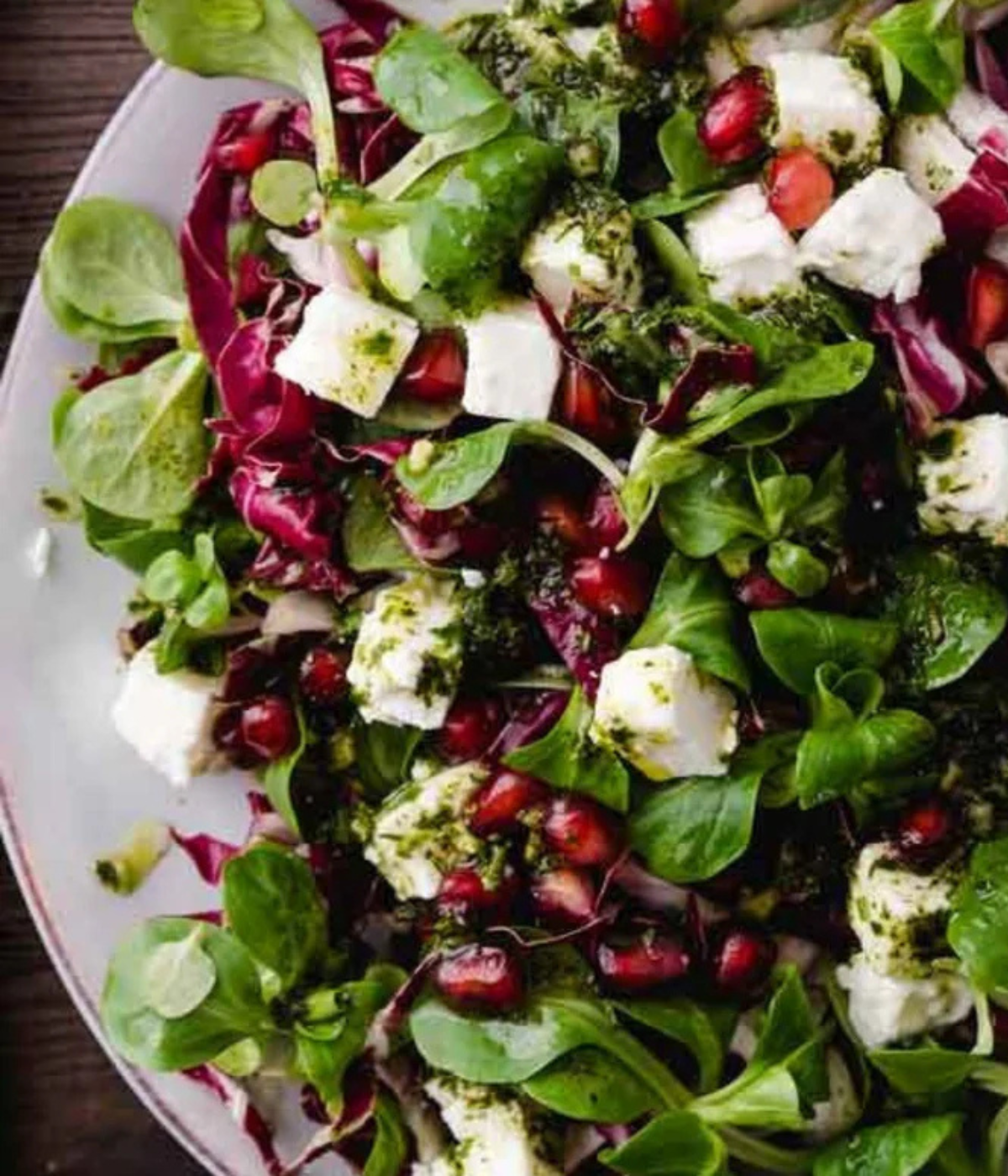 A vibrant salad of greens, radicchio, pomegranate, and feta on a white plate - presented in timeless German design by Fissler.