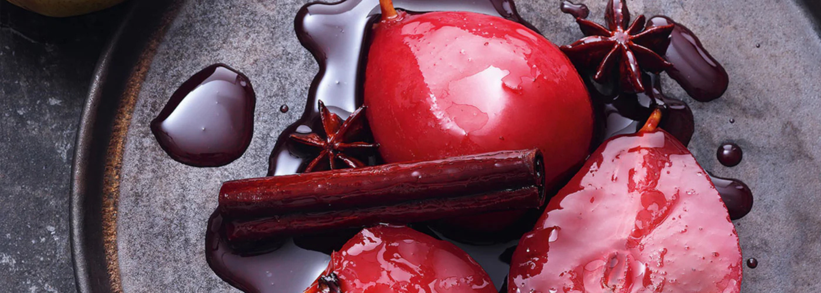 Three poached pears in red wine with star anise and cinnamon, served on a dark plate, refined with rich syrup - precisely arranged.