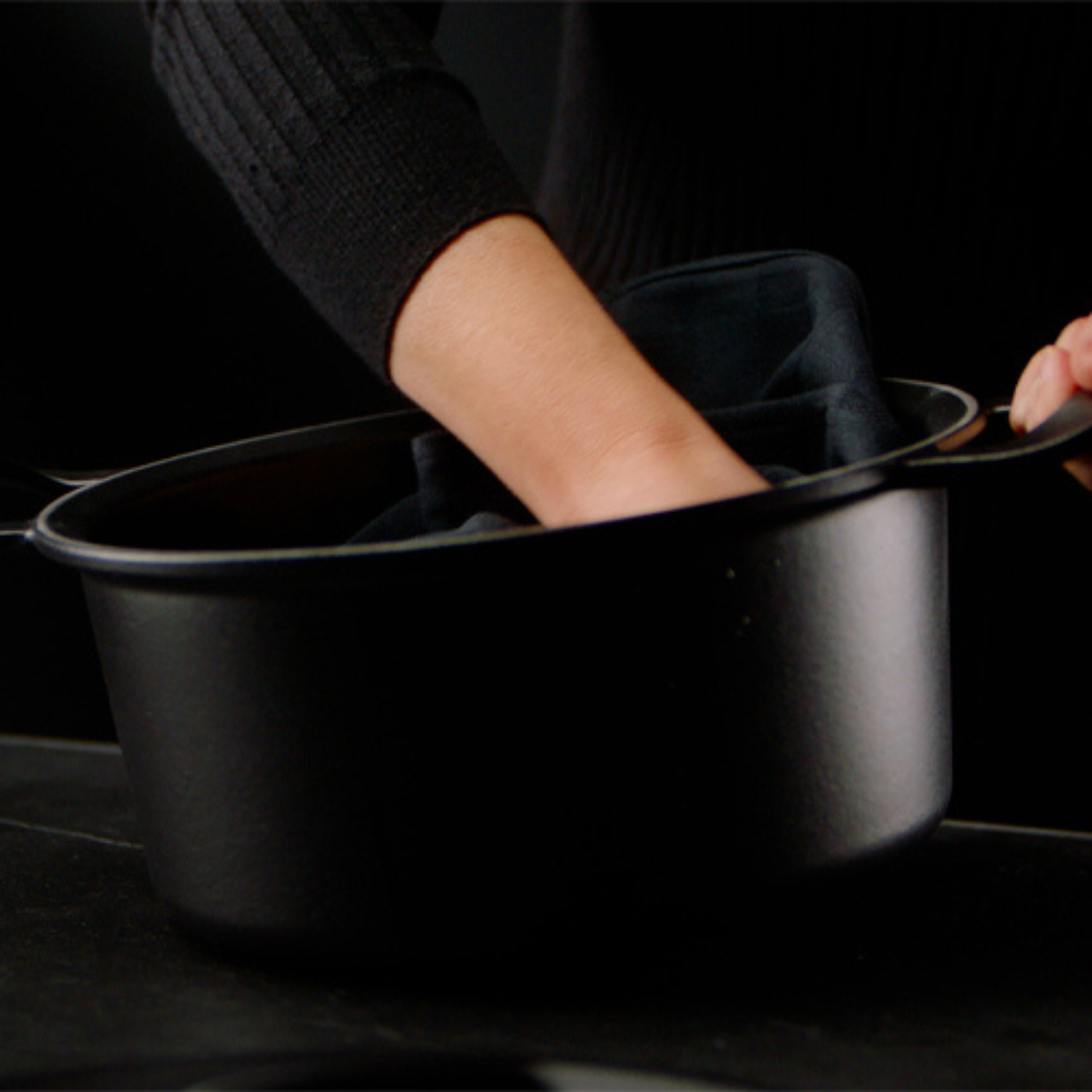 A person places a cloth into a high-quality black Fissler pot, crafted with precision on a smooth dark surface and dark background.