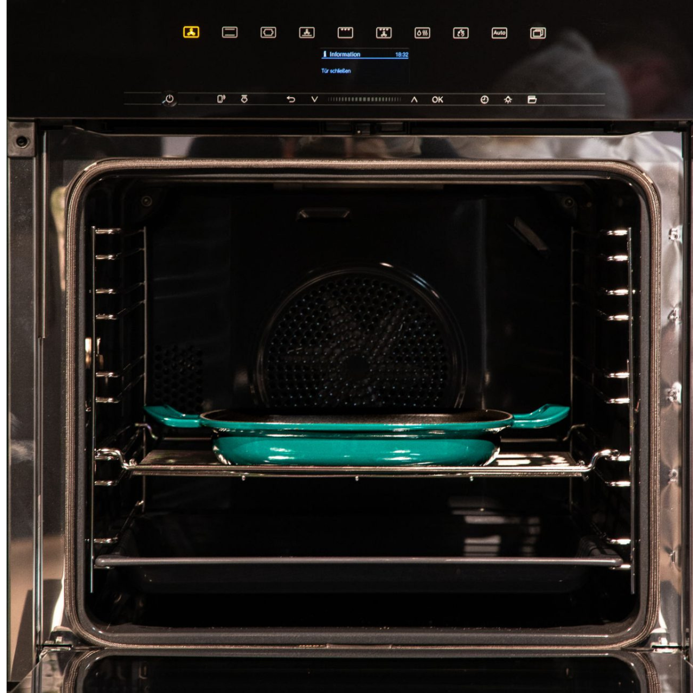 A high-quality teal Fissler baking pan, characterized by its durability and timeless design, rests in an oven beneath a digital control panel.