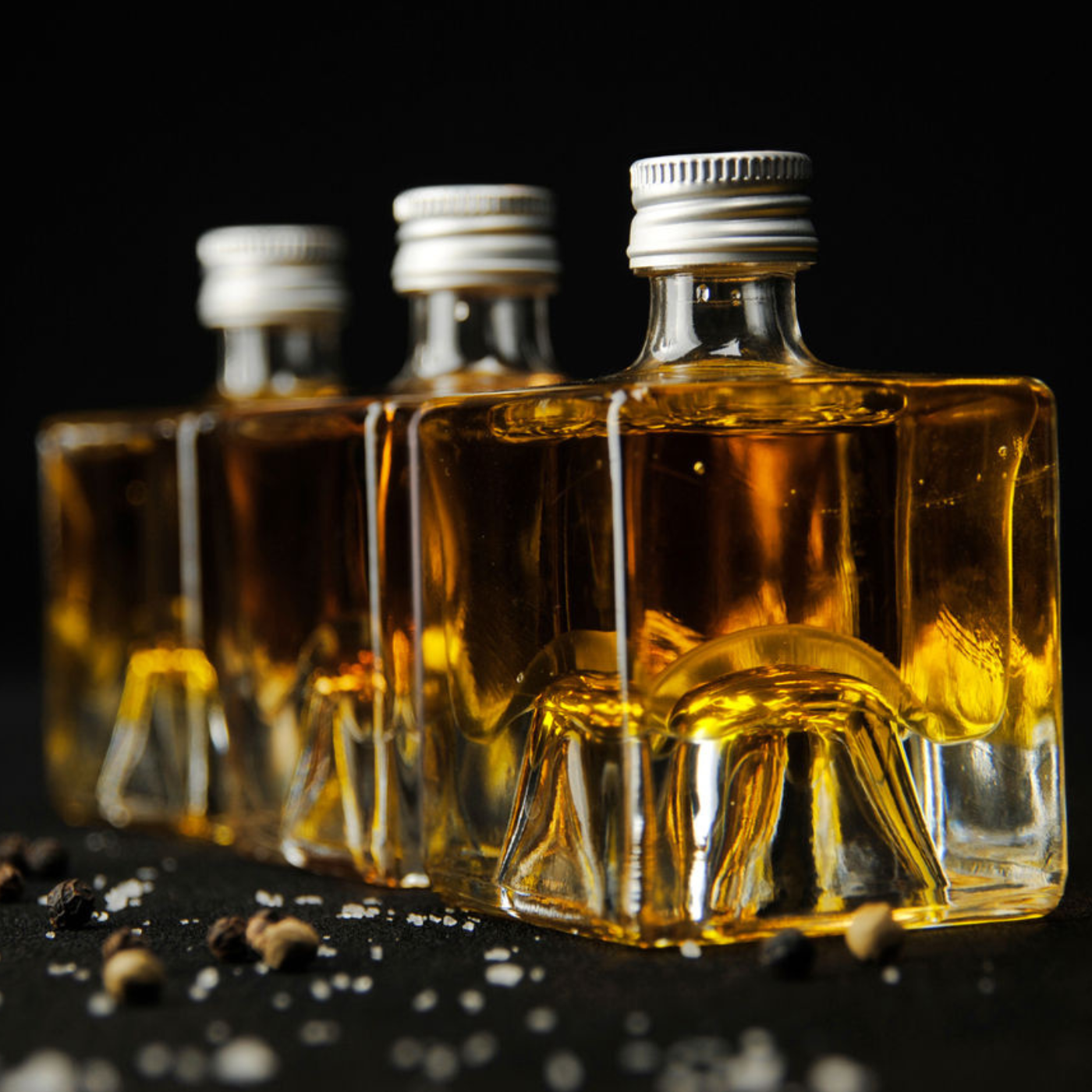 Fissler glass bottles with golden oil, silver caps, neatly arranged; peppercorns and salt crystals emphasize a refined German design.