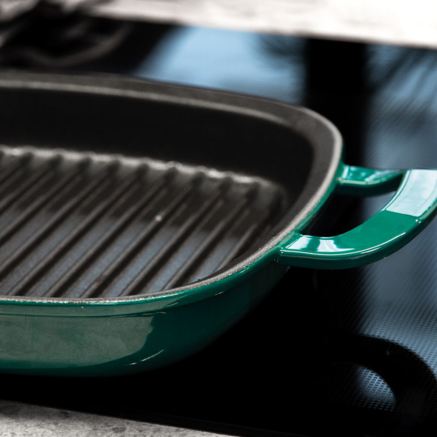 Close-up of a green Fissler cast iron grill pan with precise ridges, presented on a smooth black glass plate.