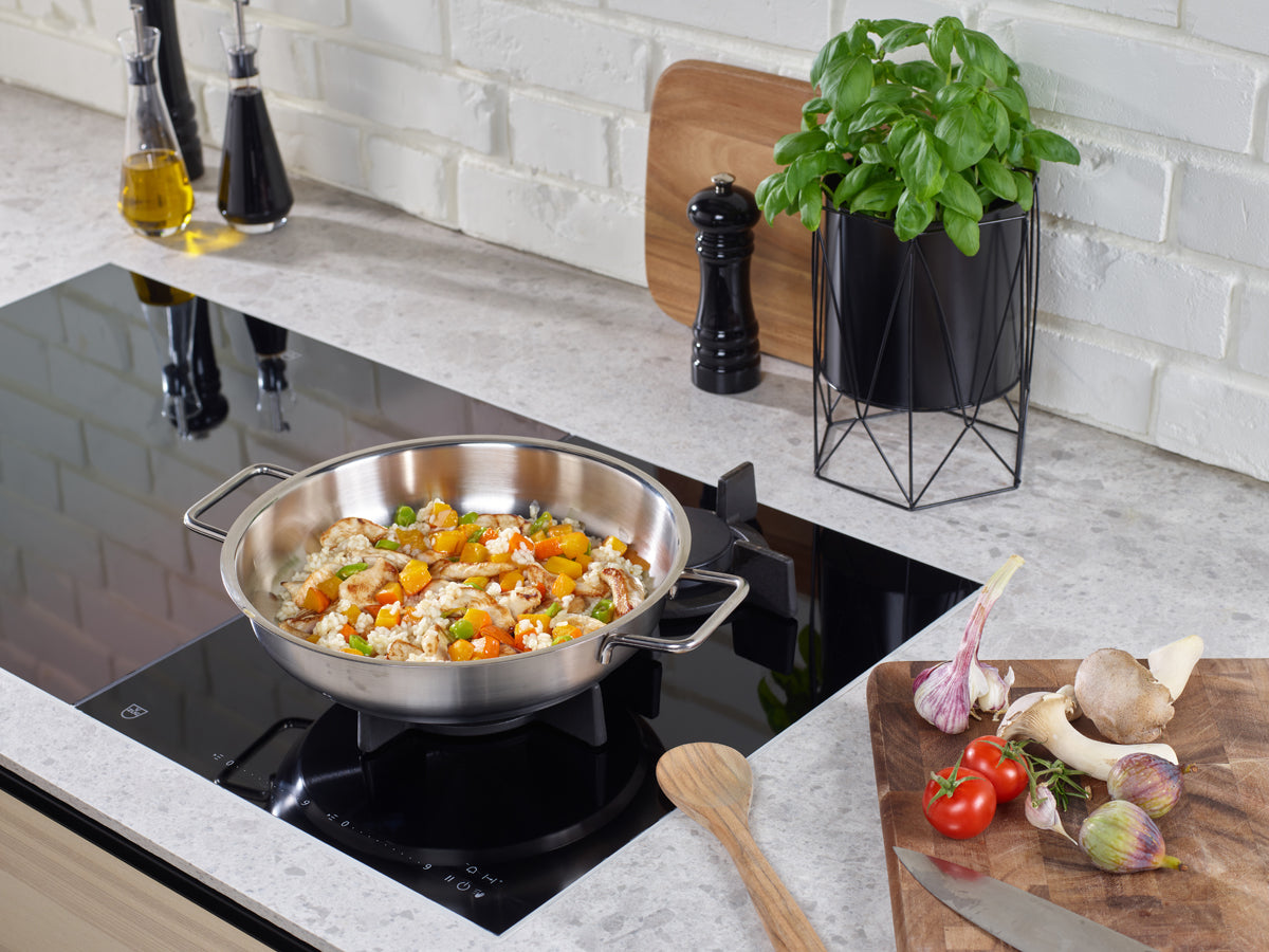 Die Fissler Pure Serving Pan, made in Germany from recycled stainless steel, cooks chicken and vegetables on a modern hob.