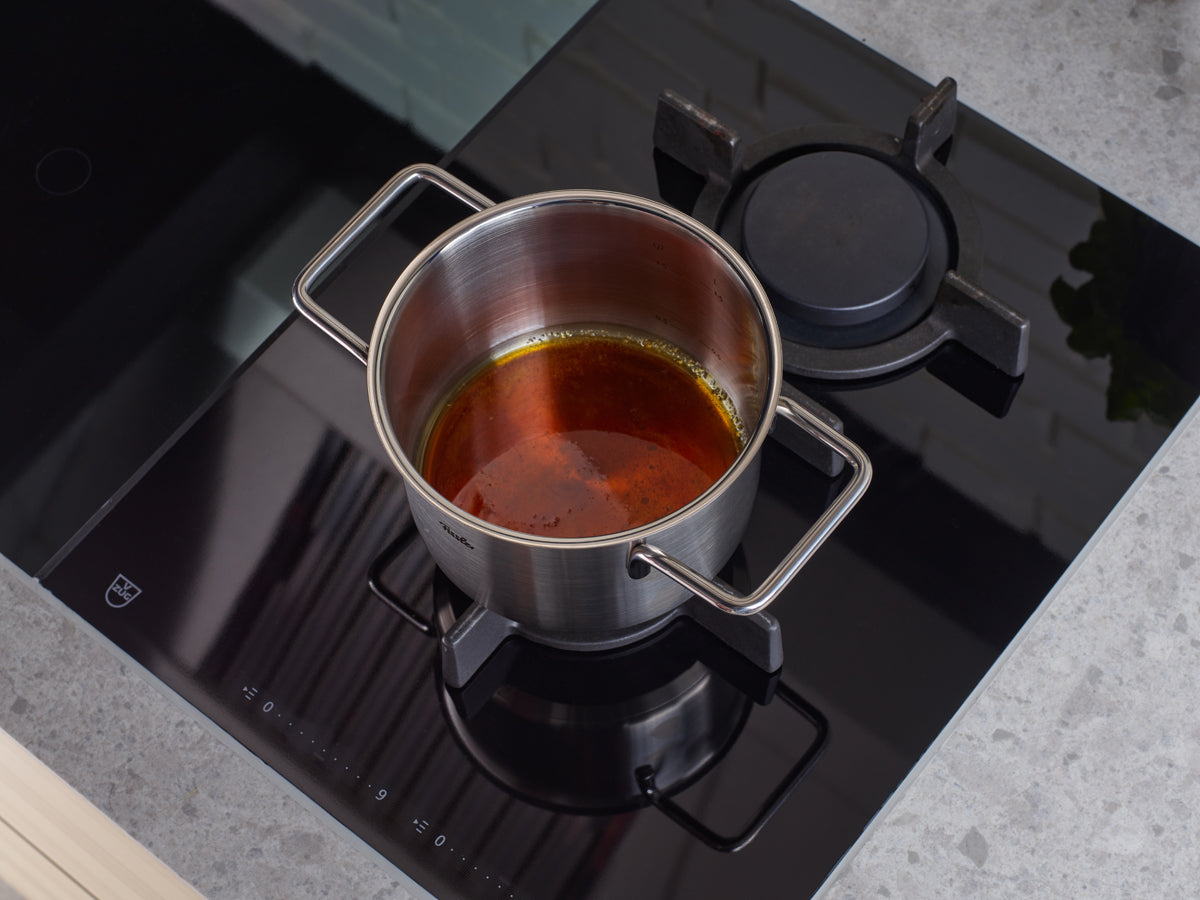 Fissler Pure Collection Kochtopf mit Glasdeckel auf Herd, ein Brenner aktiv. Präzisionskochgeschirr aus deutscher Produktion, zeitlos und langlebig.